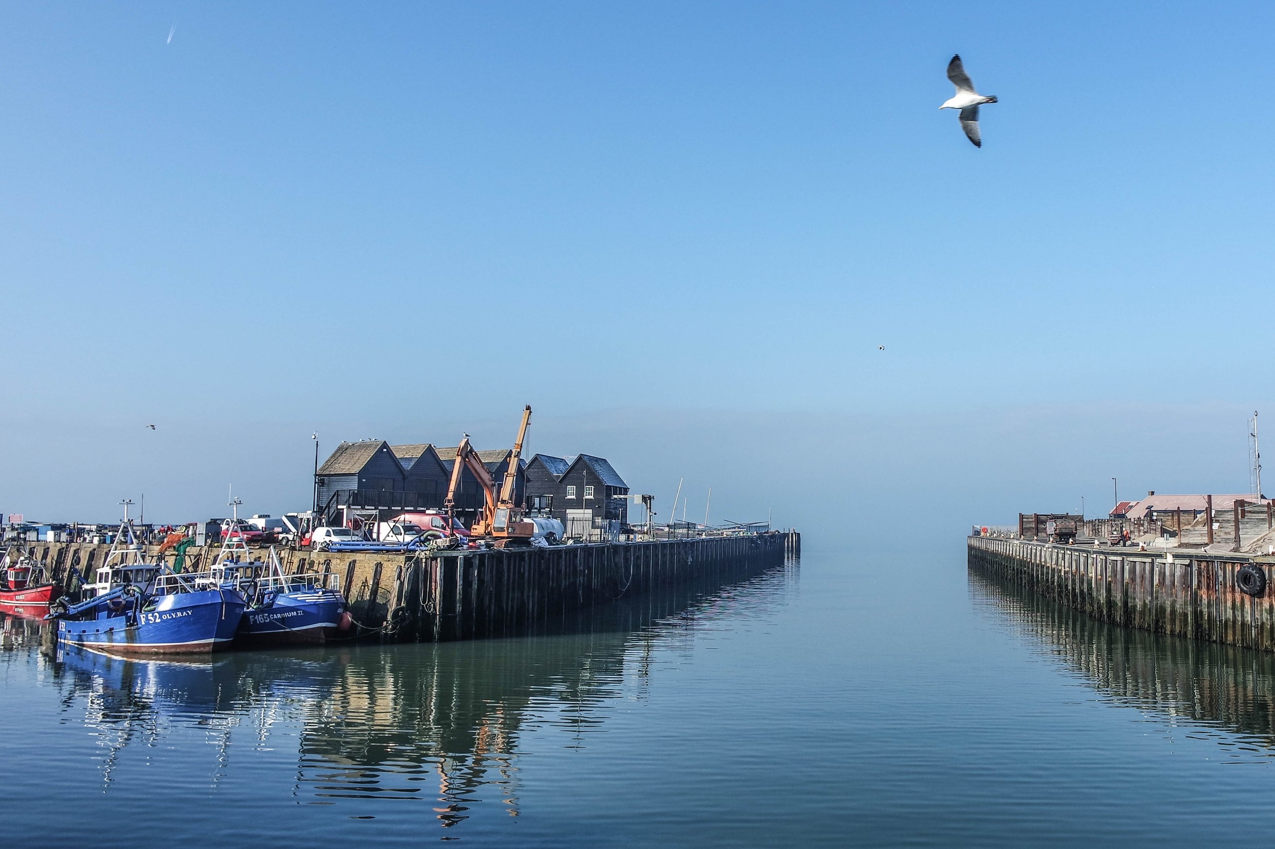 Whitstable Harbour entrance with fishing huts under a clear blue sky