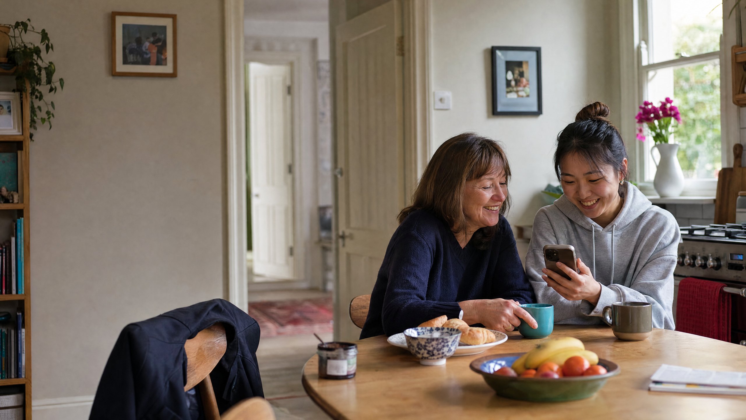 A homestay host and an international student laughing over breakfast at the kitchen table