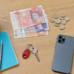 British pound notes and coins, an Oyster card, a phone, keys and a coffee on a table